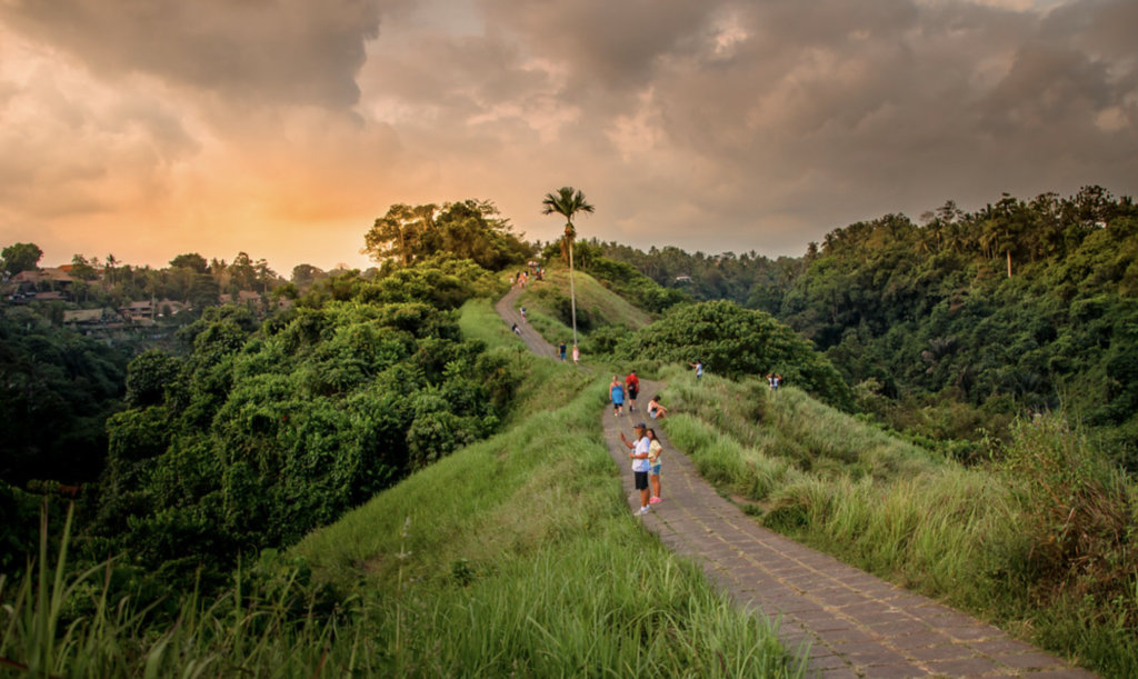 People walking along Campuhan Ridge Walk at sunset, surrounded by lush green hills and tropical forest in Ubud, Bali.