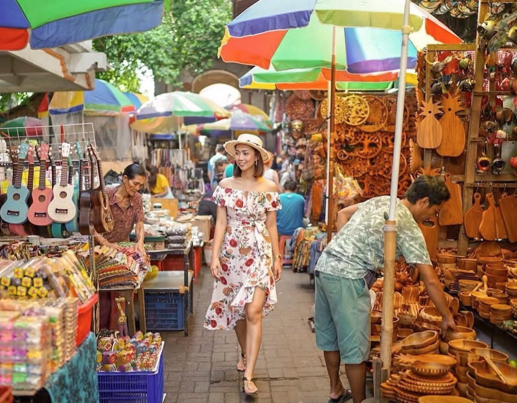 Woman walking through a colorful Ubud market with handmade crafts, wooden goods, and vibrant umbrellas.