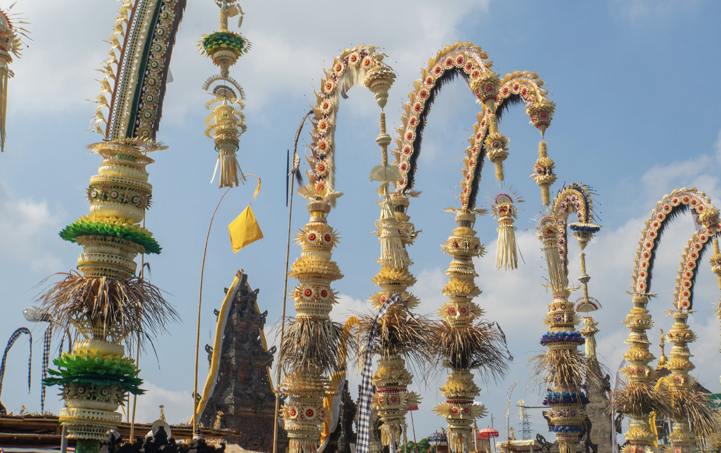 Traditional Balinese *penjor* bamboo poles decorated with intricate woven ornaments line the sky during Galungan, with temple architecture visible in the background.